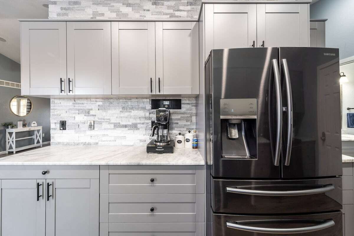 Une cuisine moderne avec des meubles gris, un réfrigérateur en acier inoxydable et une machine à café posée sur le plan de travail.