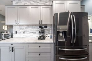 A modern kitchen with grey cabinets, a stainless steel refrigerator, and a coffee maker on the countertop.