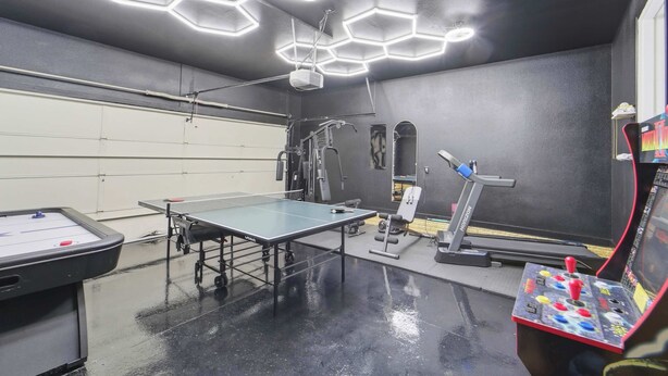 A room with a ping pong table, exercise equipment, and a projector on the ceiling.