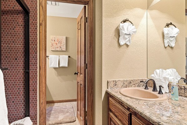 A bathroom with a wooden door, a sink with a marble countertop, and two towels hanging on the wall.
