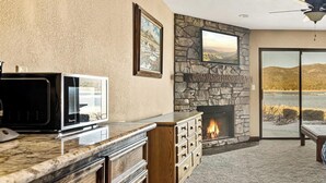 A modern kitchen with a stone fireplace, a large window overlooking a scenic view, and a ceiling fan.
