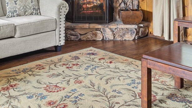 A cozy living room with a stone fireplace, wooden walls, and a floral rug.