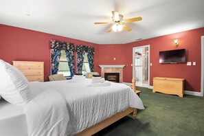 Une chambre à coucher avec un lit, un ventilateur de plafond, une cheminée, un téléviseur et une commode.