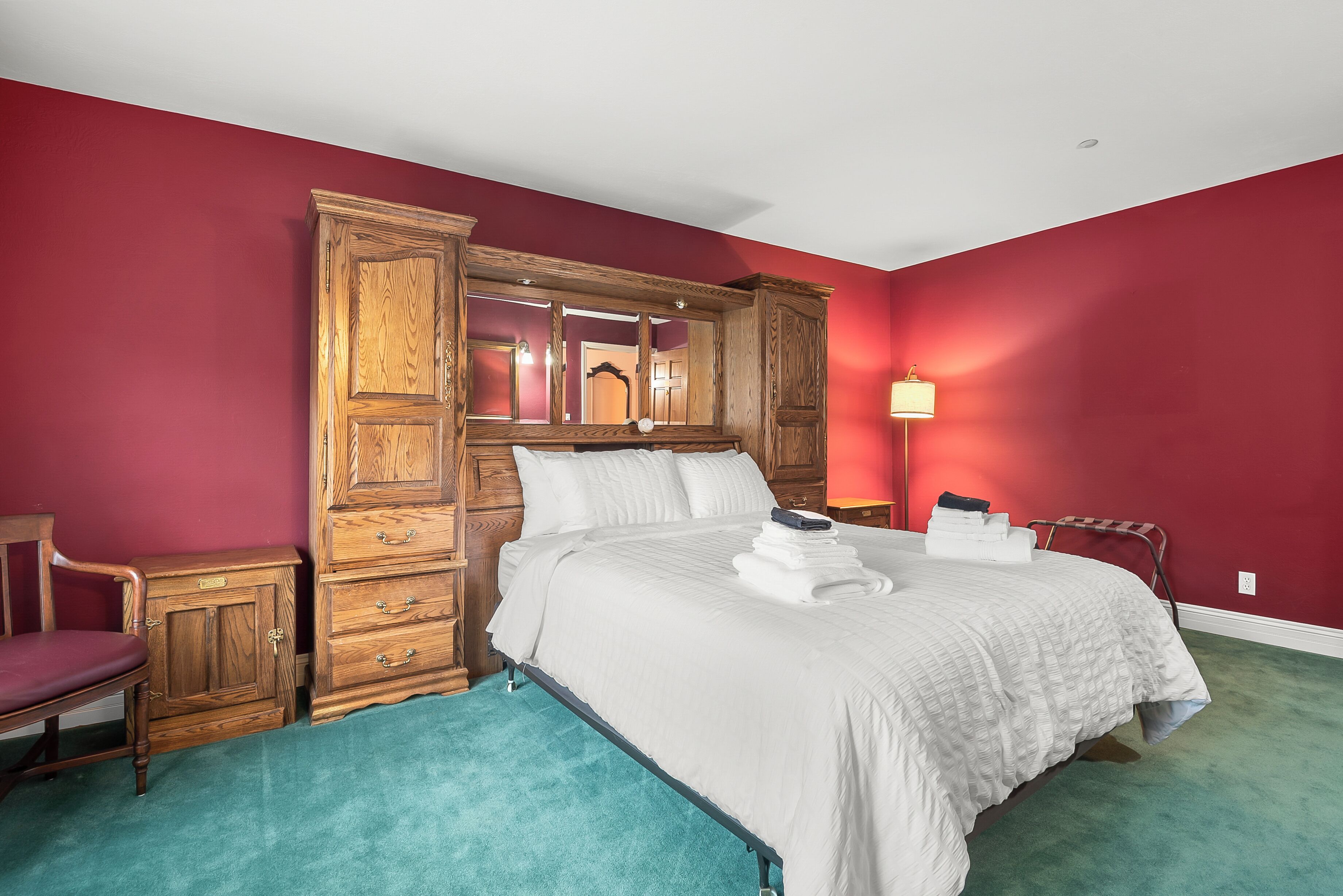 A bedroom with a large wooden wardrobe, a bed with white linens, and a teal carpet.