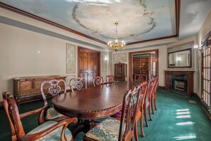 Une salle à manger élégante, avec une grande table en bois, des chaises richement décorées, un lustre et une cheminée.