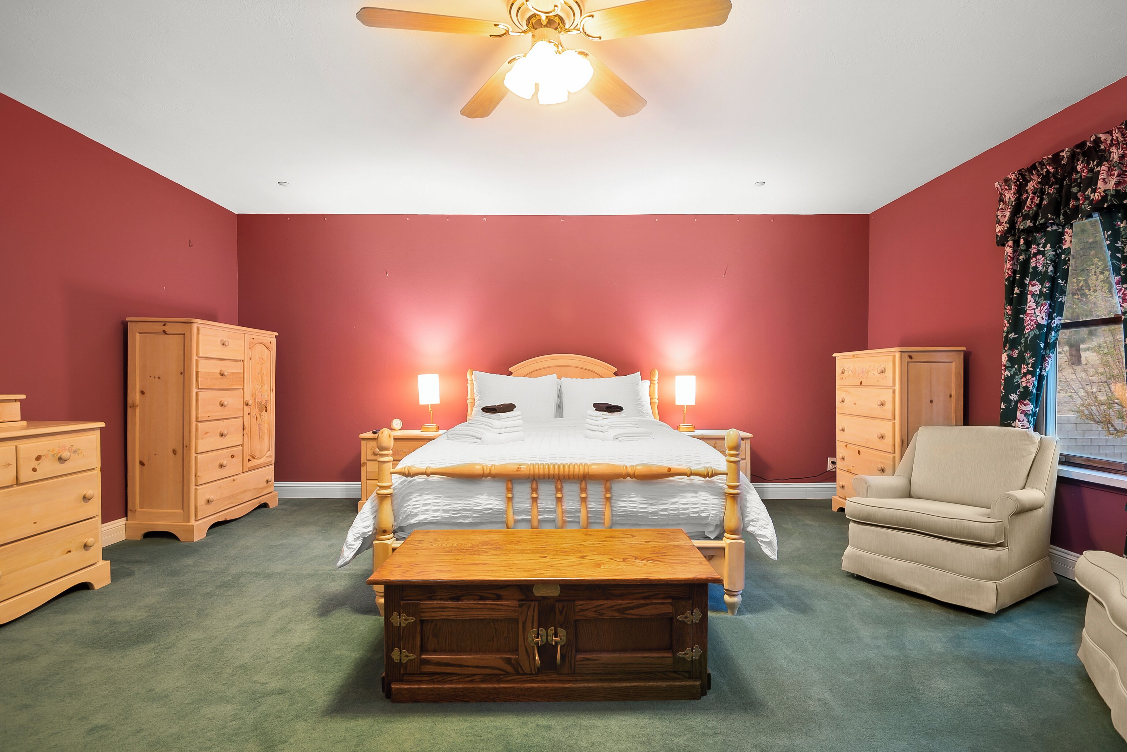 Un dormitorio con cama, muebles de madera, ventilador de techo y ventana con cortinas.