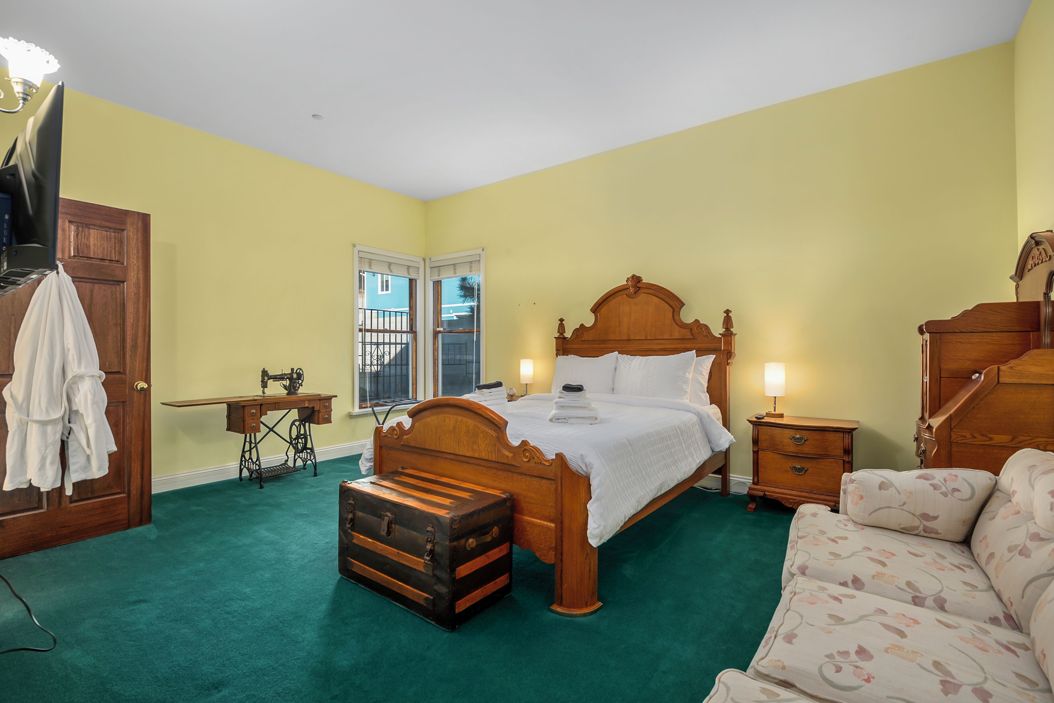Une chambre à coucher avec un lit en bois, une moquette verte, un bureau en bois et une valise.