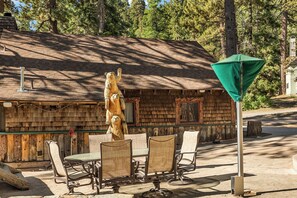 Une cabane rustique avec une façade en bois, une table à manger avec des chaises et une statue d’ours.