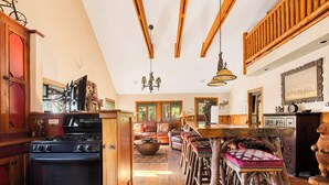A rustic kitchen with wooden beams, a large stove, and a dining area with wooden stools.