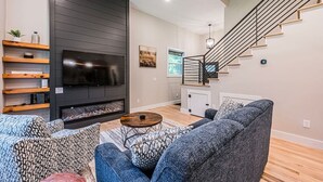 A modern living room with a fireplace, a flat-screen TV, and a staircase.