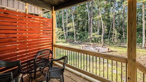 A wooden deck with a table and chairs, overlooking a forested area with a fire pit.