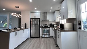 A modern kitchen with stainless steel appliances, white cabinets, and a wooden floor. - Cozy , spacious and comfortable house. Pet friendly! And close to everything!!! (Chilliwack)