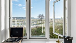 Ein Zimmer mit großem Fenster und Blick auf eine karge Landschaft mit einem einzelnen Baum.