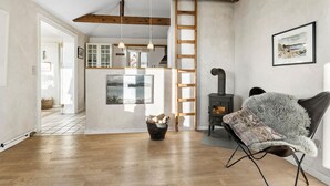 Ein gemütliches Zimmer mit Holzboden, Kamin, einer Leiter und einem Sessel mit flauschigem Überwurf.
