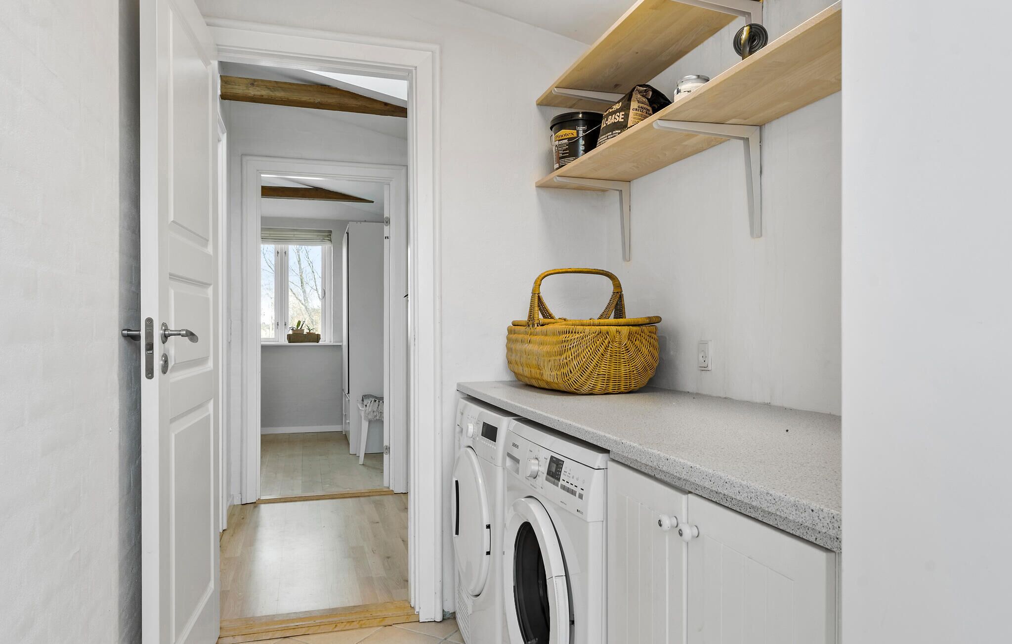 A laundry room with a washing machine, a basket, and shelves with containers.