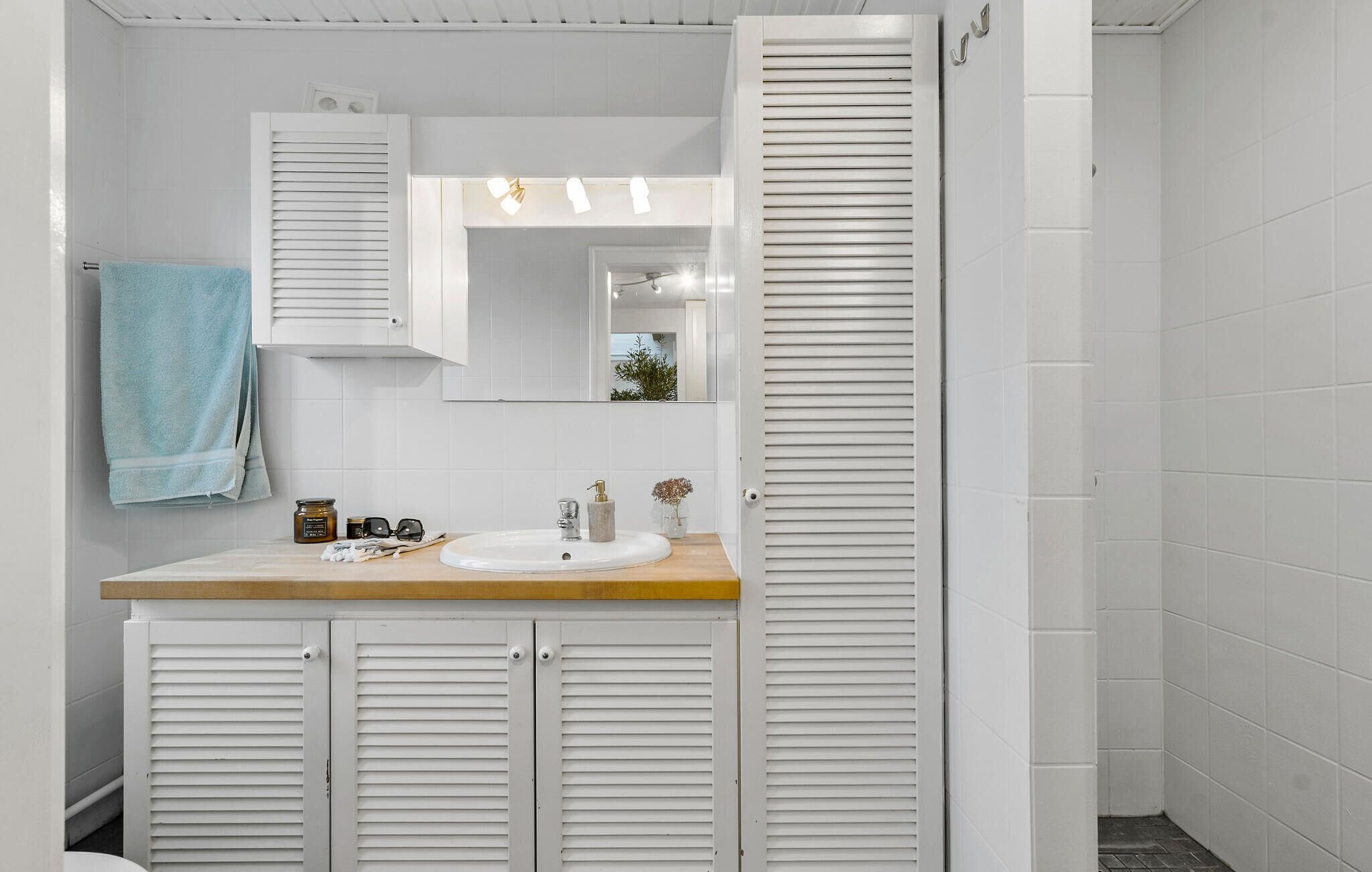 A bathroom with a white tiled wall, a wooden countertop, a sink, a mirror, and a towel hanging on the wall.