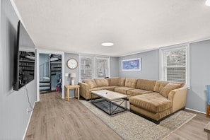 A living room with a sectional sofa, a coffee table, a TV mounted on the wall, and a staircase leading to a loft. - Student/Pet Friendly Home,Cherry Grove, Ocean Blvd (North Myrtle Beach)
