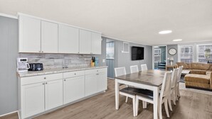A modern kitchen with white cabinets, a granite countertop, and a dining area with a wooden table and chairs. - Blue Heron, Student/Pet Friendly w/ on Ocean Blvd (North Myrtle Beach)