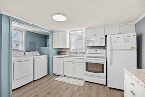 A compact kitchen with a washing machine, microwave, oven, and refrigerator.