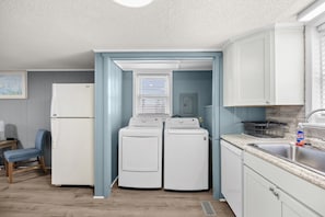 Eine kompakte Küche mit Kühlschrank, zwei Waschmaschinen, einem Spülbecken und einem Fenster mit Jalousien.