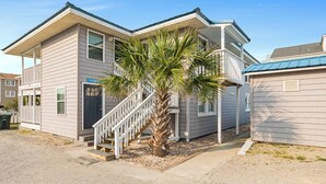 A two-story building with a staircase leading to the entrance, a palm tree in front, and a clear sky. - Blue Heron, Student/Pet Friendly w/ on Ocean Blvd (North Myrtle Beach)