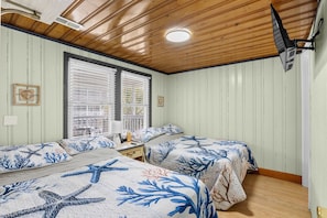 A room with two beds, a window with blinds, a ceiling fan, and a mounted television.