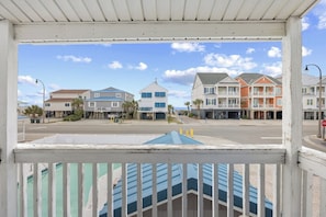 A coastal street view with multi-story buildings, a clear sky, and a pedestrian walkway.
