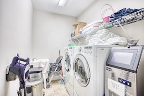 A laundry room with stacked laundry on a shelf, a washing machine, a dryer, and a folding station. - Waterfront 5 BR w/ pool & elevator Sleeps 18 (North Myrtle Beach)