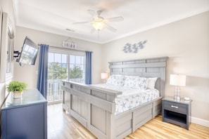 Une chambre à coucher comprenant un lit, une table de chevet, une commode, un ventilateur de plafond, une fenêtre avec des rideaux et une vue sur l’extérieur.