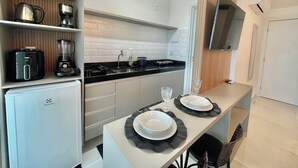 Una cocina moderna con lavavajillas integrado, cafetera y licuadora sobre la encimera. Hay una mesa pequeña con platos y una copa.
