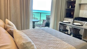 Habitación de hotel con cama, una mesa de comedor con sillas, zona de cocina y balcón con vistas al océano.