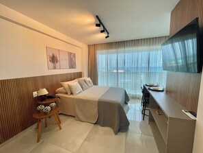 Ein Hotelzimmer mit Bett, Schreibtisch, Stuhl, Lampe, Fernseher und einem Fenster mit Vorhängen.