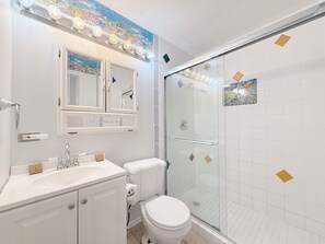 A bathroom with a glass-enclosed shower, a white sink, and a toilet. - Spacious-Beachfront Condo with WiFi, Pool, Tennis, AC (St Thomas)