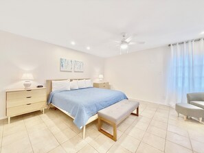 A bedroom with a bed, bedside tables, a bench, a ceiling fan, and artwork on the wall. - Spacious-Beachfront Condo with WiFi, Pool, Tennis, AC (St Thomas)