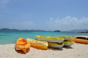 A beach with several kayaks lined up on the sand, a clear blue sky, and distant mountains. - Spacious-Beachfront Condo with WiFi, Pool, Tennis, AC (St Thomas)