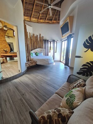 Relax in a spacious room with a large bed, sofa, and television, surrounded by natural light and a decorative leaf.