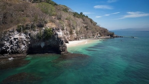 Eine Küstenlandschaft mit klarem türkisblauem Wasser, einem Sandstrand und felsigen Klippen.