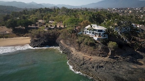 Ein Küsteneigentum mit einem Haus auf einer Klippe mit Blick auf das Meer, umgeben von viel Grün und Bergen in der Ferne.