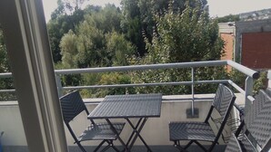 Een balkon met een tafel en vier stoelen, met uitzicht op een tuin met bomen en een gebouw op de achtergrond.