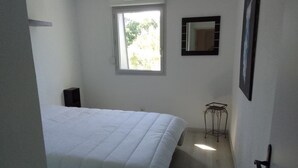 Een slaapkamer met een bed, een raam, een spiegel en een kleine tafel.