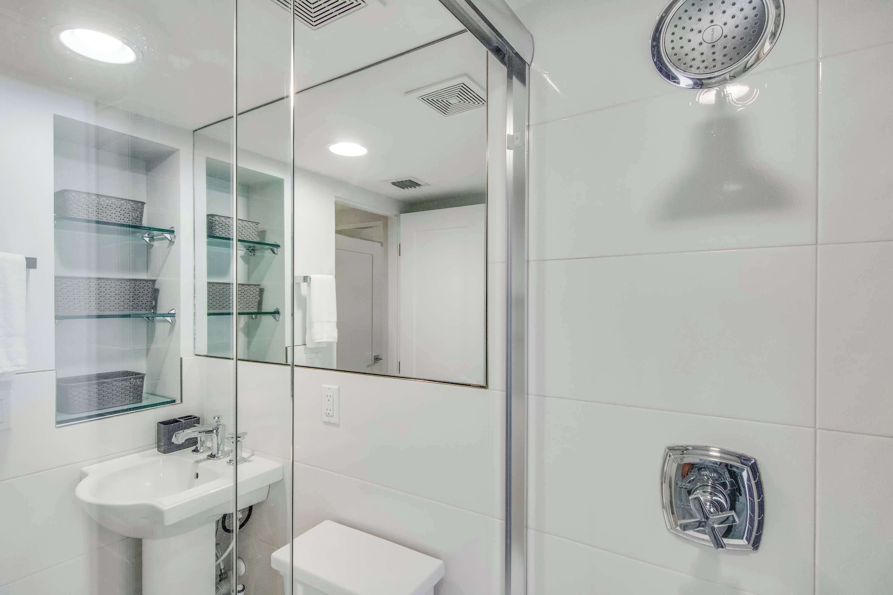 Een moderne badkamer met een glazen douchecabine, een witte wastafel en een glazen schapunit.
