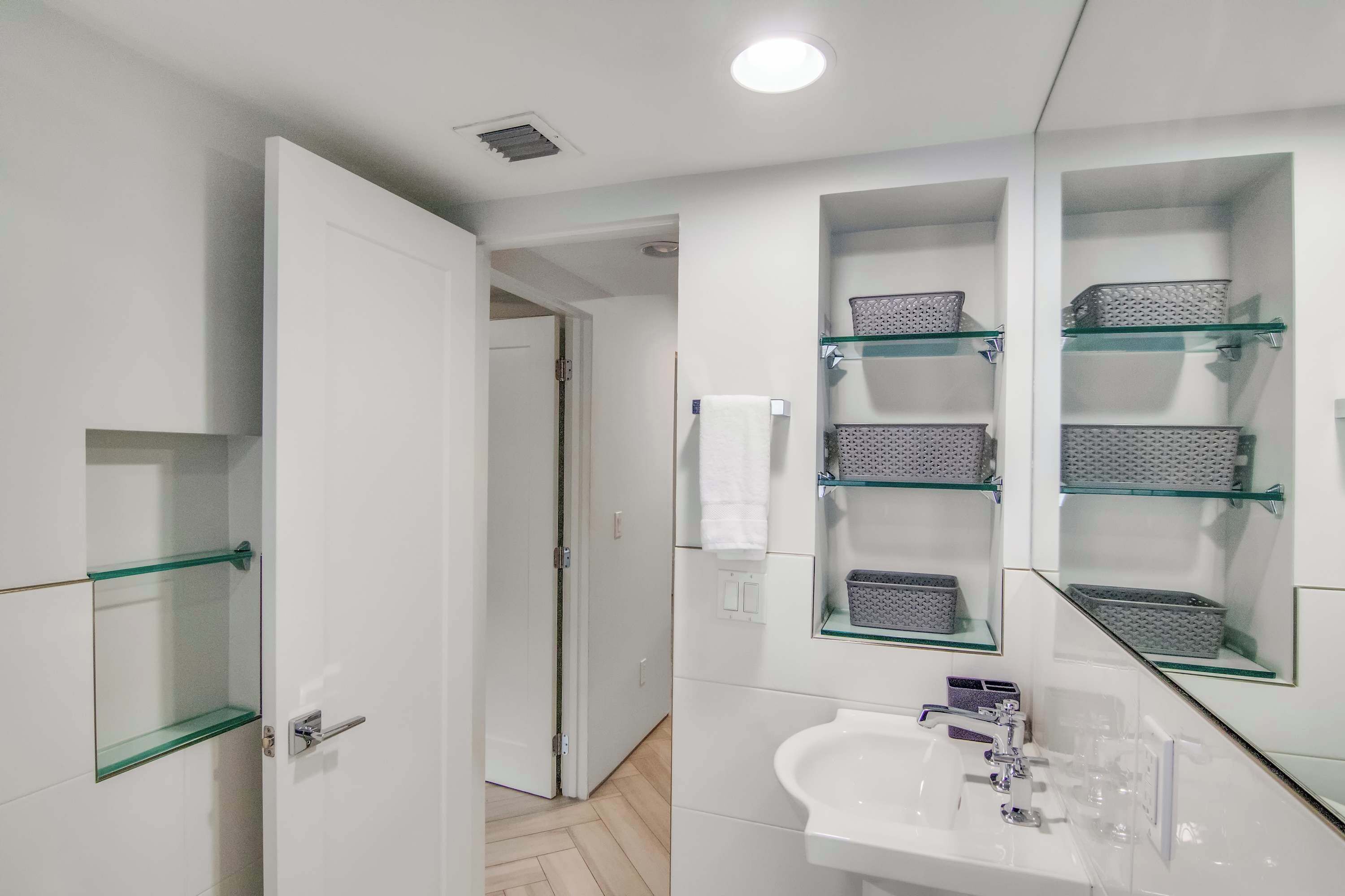 Une salle de bain moderne avec une étagère en verre, un lavabo blanc et un miroir.