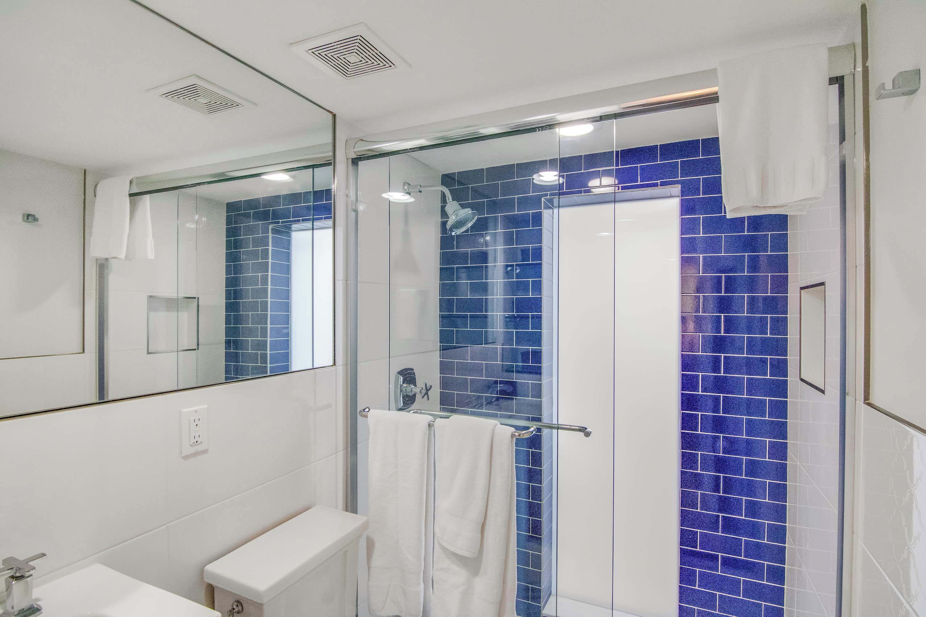 Een moderne badkamer met een douchecabine van glas, witte sanitair en blauwe betegelde wanden.