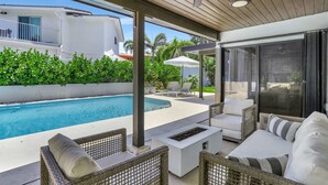 An outdoor pool area with wicker furniture, a ceiling fan, and a view of a white building.