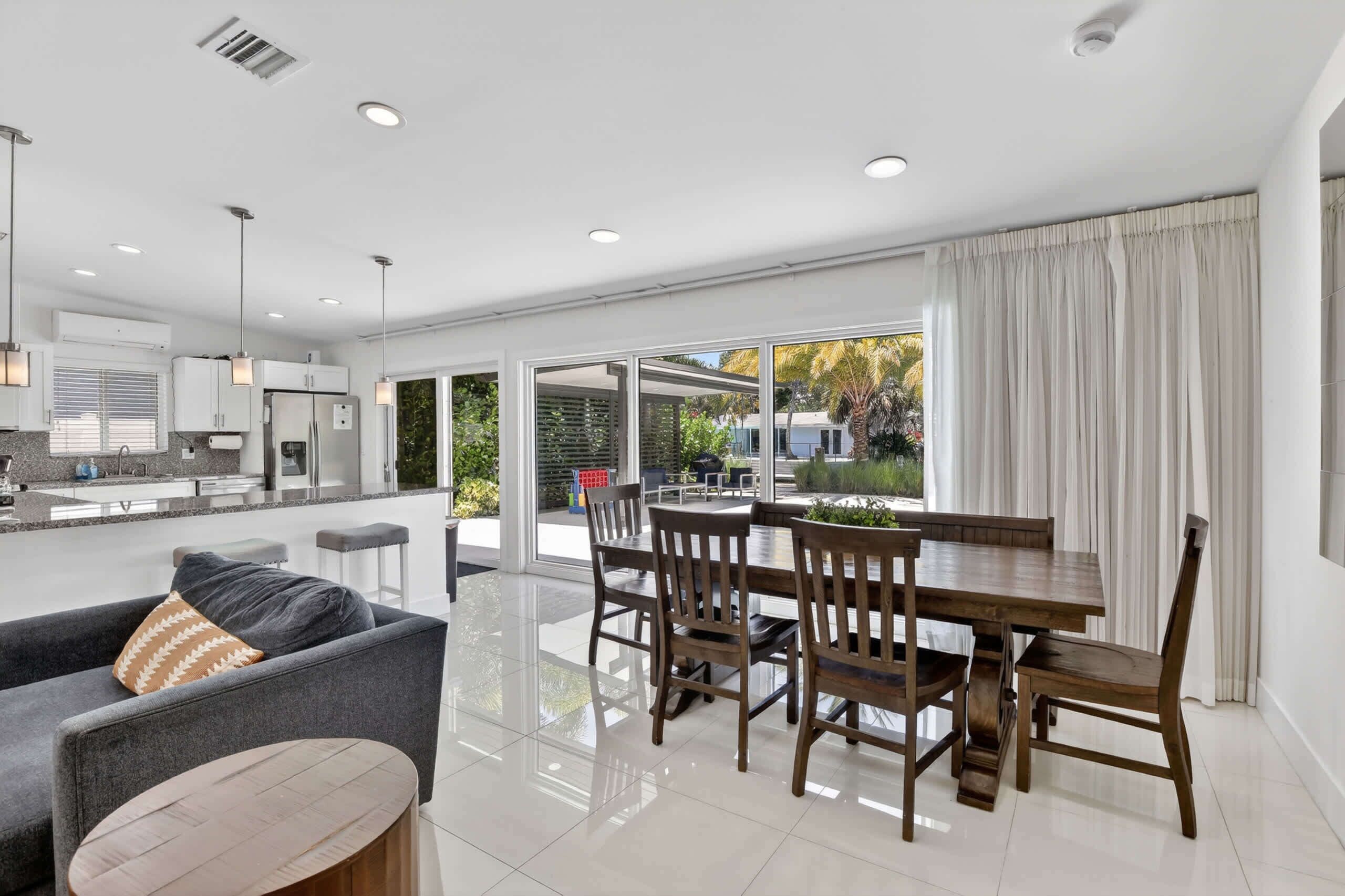 A modern kitchen with white cabinets, a dining area with a wooden table and chairs, and a large sliding glass door leading to an outdoor patio.