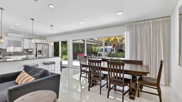 A modern kitchen with white cabinets, a dining area with a wooden table and chairs, and a large sliding glass door leading to an outdoor patio.