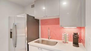 Una cocina con armarios blancos, un refrigerador de acero inoxidable, un lavamanos y un salpicadero con diseño rojo.