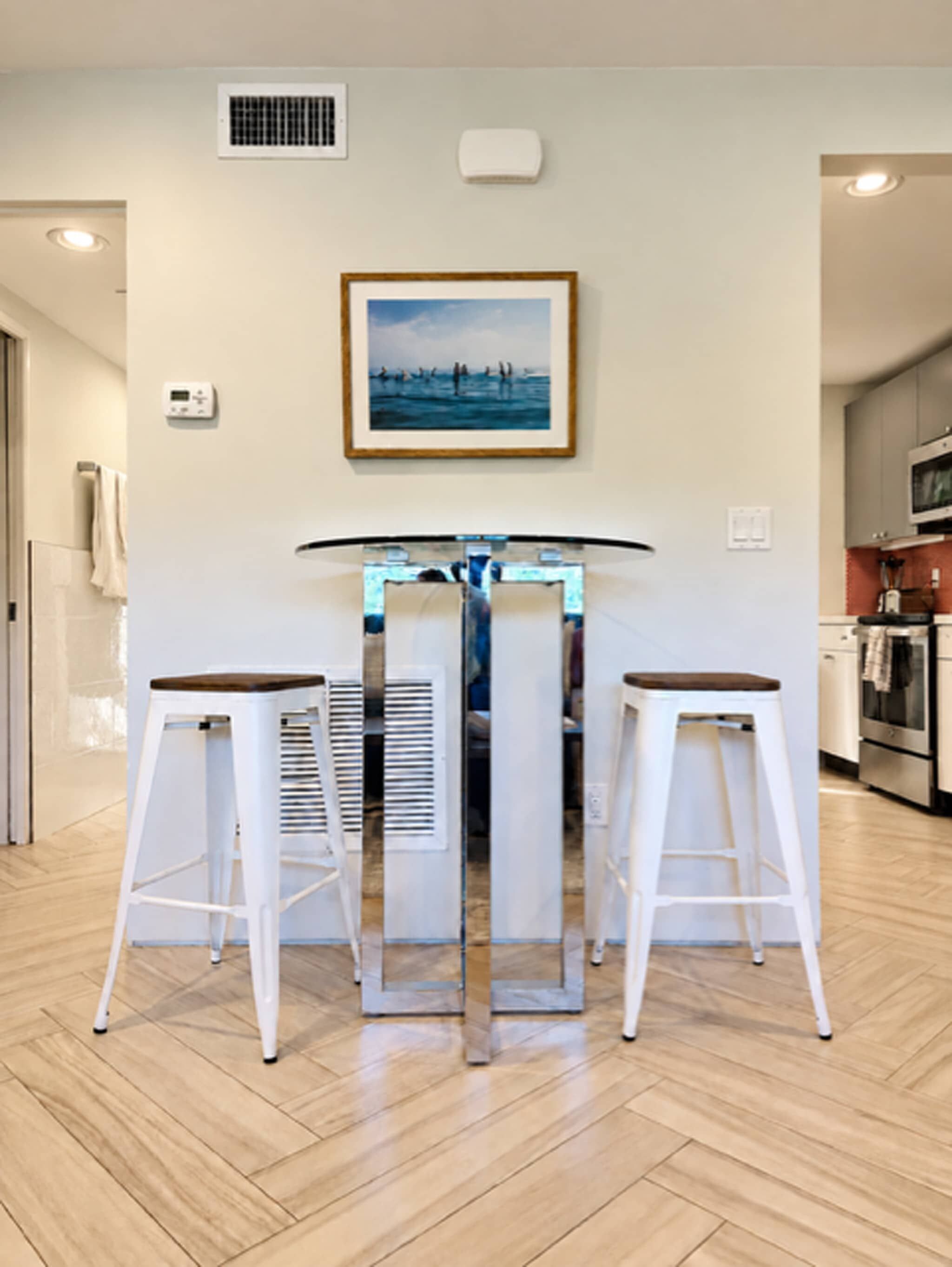 A modern kitchen with a central island, white bar stools, and a framed picture on the wall.