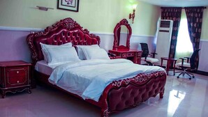 A large, ornate bed with a red headboard and white bedding in a hotel room. - Greatwood Hotel (Owerri)