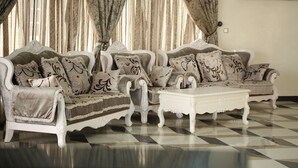 A room with a checkered floor, a white sofa set with patterned cushions, and a white coffee table. - Greatwood Hotel (Owerri)